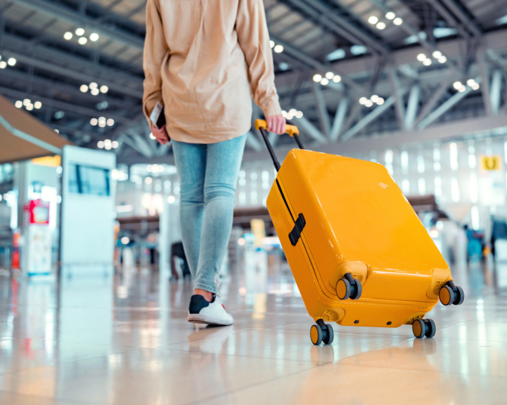 Close up shot of young woman carrying yellow suitcase through airport.